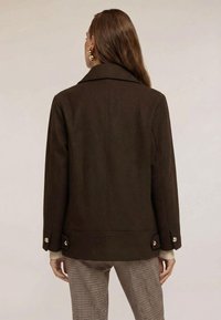 Ruskea villasekoitejakku lovikauluksella, napitetuilla kalvosimilla ja suoralla leikkauksella. Sileä pinta, jossa näkyvät ompeleet.