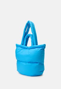 Saco tote azul em puffer com uma textura suave e almofadada. Apresenta duas alças grossas e torcidas, e uma forma arredondada e flexível.