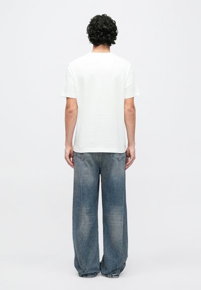 Biele tričko s krátkym rukávom v kombinácii s voľnými, vyblednutými modrými džínsami. Materiál pôsobí mäkko s hladkou textúrou. Jednoduchý dizajn.