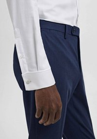 Witte dress shirt manchet met afgeronde randen, voorzien van een enkele knop. Gepaard met donkerblauwe broek, met een gladde textuur en een op maat gemaakte pasvorm.