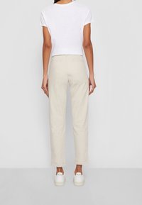 Pantalon beige taille haute avec une coupe droite, doté de deux poches arrière. Associé à un t-shirt blanc à manches courtes et des baskets blanches.