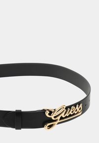 Cintura in pelle nera con una texture liscia, caratterizzata da un prominente logo dorato "Guess" come dettaglio della fibbia laterale. Regolabile con buchi.