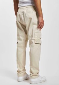 Beige cargo pants with an elastic waistband, side pockets, and button accents, made of a textured cotton material. Worn with white sneakers.