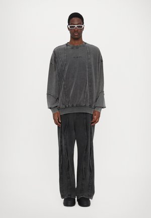 Übergroßer, dunkelgrauer Sweatshirt mit gestickten Details, kombiniert mit passenden, dunkelgrauen weit geschnittenen Hosen und schwarzen Schuhen. Weiche Textur, minimalistisches Design.
