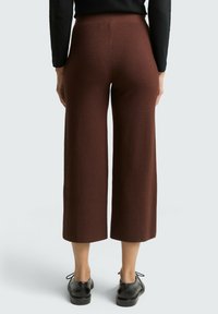 Bruine wijde broek van zachte stof, met een middelhoog taille en een gladde textuur. Gecombineerd met zwarte schoenen.