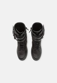 Stivali da combattimento in pelle nera con design a collo alto, chiusura con lacci e dettagli con fibbie. Suola in gomma testurizzata con motivo a zigzag.