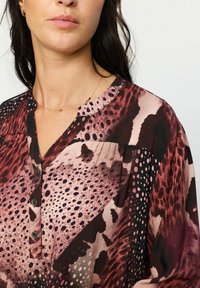 Knapp-up bluse med et flerfarget mønster i nyanser av burgunder, svart og rosa. Myk stoff, V-hals og synlige knapper.