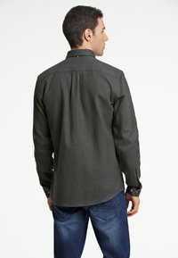 Donkergrijze blouse met lange mouwen en een button-down kraag, zichtbare stiksels en knoopsluiting bij de mouwen. Geverfd stof, rechte zoom en detail met rugplooien.