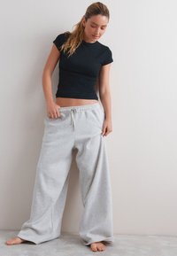 Black fitted T-shirt paired with light gray, loose-fitting sweatpants with an elastic waistband and drawstring. Smooth fabrics, casual look.