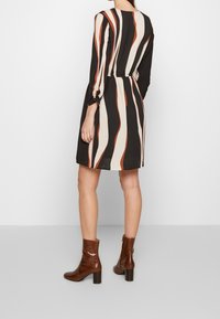 Schwarzes Kleid mit vertikalen cremefarbenen und rostbraunen Streifen, langen Ärmeln mit gerafften Manschetten und tailliertem Schnitt. Tragen mit braunen Ankle Boots aus Krokoleder.