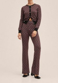 Conjunto coordinado que presenta un cárdigan de diseño recortado en patrón negro y rojo con mangas largas, combinado con pantalones ajustados a juego.