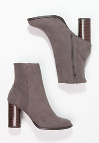 Botas de tobillo de ante gris con un alto tacón de madera estriado y una cremallera lateral. Textura suave y forma moderna y elegante.