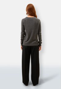 Szary wełniany sweter z okrągłym dekoltem, długimi rękawami i gładką teksturą, w połączeniu z szerokimi czarnymi spodniami. Czysty i minimalistyczny design.