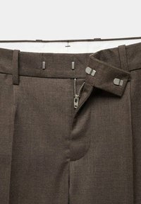 Pantaloni marroni su misura con una superficie liscia, zip frontale e vita con doppio gancio. Linee pulite con passanti per cintura e minimi dettagli hardware.