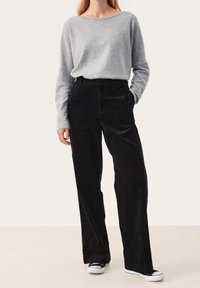 Pull gris tricoté à manches longues, associé à un pantalon large en velours côtelé noir taille haute et des baskets en toile noires.