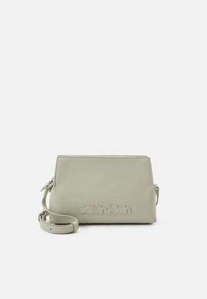 Lysegrå rektangulær Calvin Klein crossbody taske med justerbar rem og præget brandlogo på frontens midte.