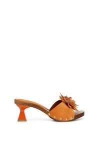 Sandalia deslizante de ante en naranja con suela de madera. Presenta un acento floral y tachuelas plateadas a lo largo de la tira. Tacón esculpido en naranja.