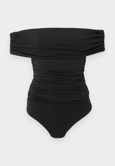 Juodas off-shoulder ruošiniai bodysuit su spaustukais kirkšnies srityje, išdėliotas ant balto fono.
