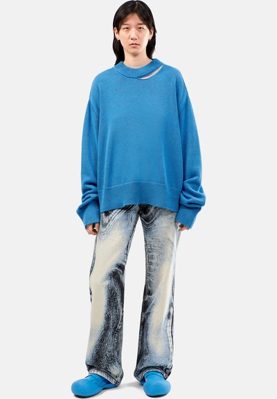 Blue oversized sweater, loose-fitting light jeans with dark swirls, and blue footwear; features a cutout at the neckline.