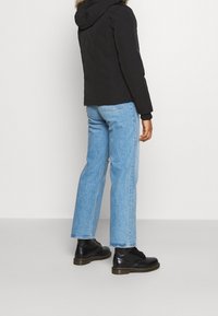 Svart vadderad jacka med huva, i kombination med ljusblå raka jeans av denim och svarta snörkängor. Enkelt design, inga synliga mönster.