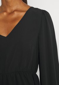 Schwarzes Kleid mit V-Ausschnitt, langen Puffärmeln und elastischem Bund. Es verfügt über einen glatten, leichten Stoff mit minimalen Nahtdetails.