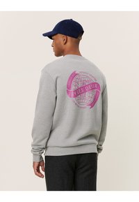 Szary sweatshirt z okrągłym dekoltem i ściągaczami. Z tyłu widnieje różowa grafika globu z napisem "BY LES DEUX" oraz dekoracyjnymi wstążkami.