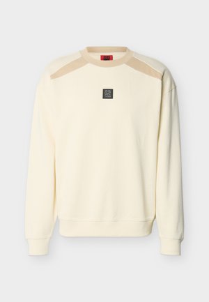 Felpa a maniche lunghe color crema con accenti beige sulle spalle e una piccola toppa con logo quadrato nero al centro del petto.