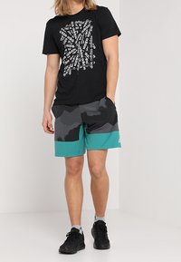 Černé tričko s bílým motivem, šedé maskáčové šortky s tyrkysovými akcenty a černé tenisky. Ležérní sportovní oblečení vhodné pro venkovní aktivity.