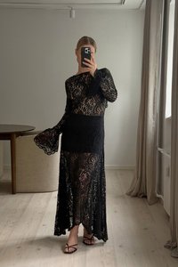 Juoda nėriniuota maxi suknelė su ilgomis rankovėmis, sudėtingais gėlėtais raštais, prigludusia liemene ir laisvu sijonu. Įvaizdį užbaigia šlepetės.