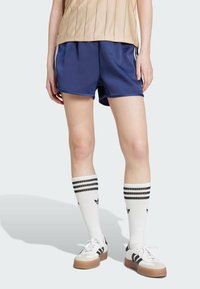 Mornarske sportske kratke hlače glatke teksture, s bijelim bočnim trakama, uparene s bijelim čarapama do koljena koje imaju crne pruge i logo, te tenisicama.