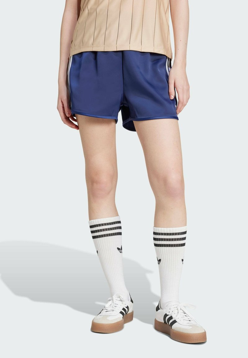 Mornarske sportske kratke hlače glatke teksture, s bijelim bočnim trakama, uparene s bijelim čarapama do koljena koje imaju crne pruge i logo, te tenisicama.