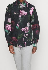 Camicia nera con motivo floreale che presenta fiori rosa e viola con foglie verdi; maniche lunghe, colletto a punta, realizzata in tessuto leggero.