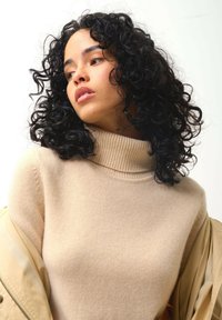 Beige Strickrollkragenpullover mit geripptem Kragen, getragen unter einer hellbeigen Oberbekleidung; zeichnet sich durch eine weiche Textur und eine fitte Passform aus.