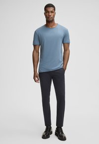 T-shirt bleu à manches courtes avec un col rond, associé à un pantalon slim noir. Des chaussures noires à lacets complètent la tenue.