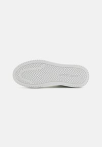 Semelle de chaussure blanche avec un motif de semelle en zigzag, présentant une texture lisse et des bords ronds. Nom de la marque visible en lettres en relief.
