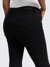 Černé džíny vyrobené z měkkého denimu, s úzkým střihem, dvěma zadními kapsami a štítkem na pásku. Tkanina má hladkou, elegantní strukturu.