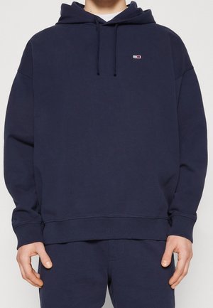 Sweatshirt bleu marine en tissu doux, avec une capuche à cordon, des poignets côtelés et un petit logo sur la poitrine.