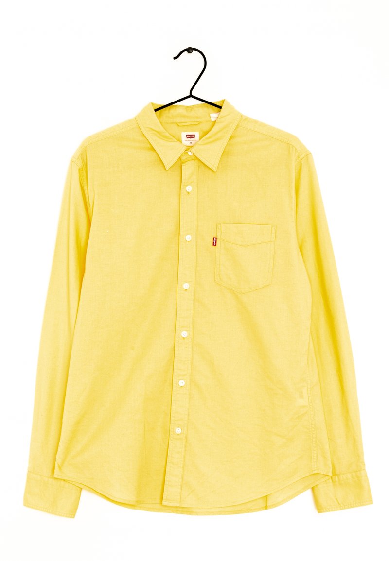Chemise jaune à manches longues avec boutons, col et poche poitrine suspendue sur un cintre noir sur fond blanc.
