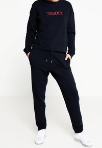Sudadera de algodón azul marino con bordado rojo "T.O.M.M.Y.", combinada con joggers a juego que tienen una cinta elástica en la cintura y cordón.