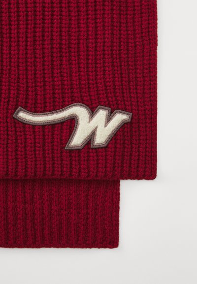 Sciarpa rossa lavorata a maglia realizzata in lana spessa, con un logo in tessuto crema bordato di marrone su un'estremità. Design a coste testurizzato in tutta la lunghezza.