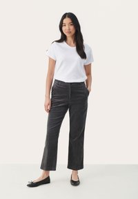 T-shirt blanc à manches courtes, pantalon en velours côtelé noir avec des rayures verticales, et ballerines noires. Modèle debout avec les mains dans les poches.
