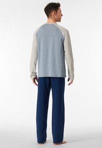Camicia a maniche lunghe con corpo blu e maniche grigie, abbinata a pantaloni larghi blu navy. Tessuto morbido con texture liscia.