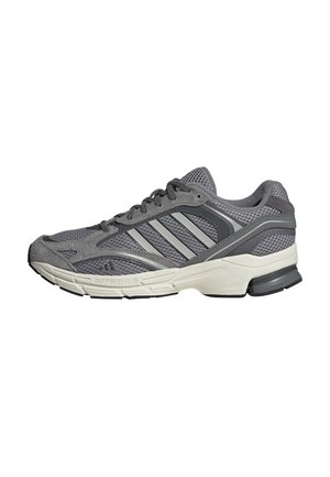 Zapatilla deportiva gris y negra con suela blanca, parte superior de malla y ante, cierre con cordones y tres franjas diagonales en el lateral.