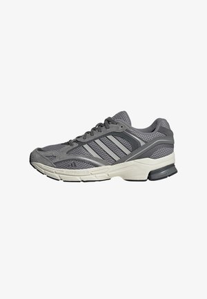 Zapatilla deportiva gris y negra con suela blanca, parte superior de malla y ante, cierre con cordones y tres franjas diagonales en el lateral.