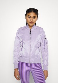 Levanduľová bomber bunda so zipsom, bočnými vreckami a ribbed lemom. Na rukáve je detail loga v kontrastnej farbe.