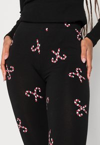 Leggings noirs avec un motif de cannes en sucre à rayures rouges et blanches. Le tissu semble extensible et lisse, conçu pour un port décontracté.