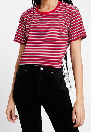 T-shirt court à rayures rouges avec des rayures blanches et noires, col rond et manches courtes, associé à un pantalon taille haute en velours côtelé noir.