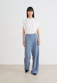Haut blanc à manches courtes associé à un pantalon large bleu clair en tissu lisse. Des chaussures noires complètent la tenue.