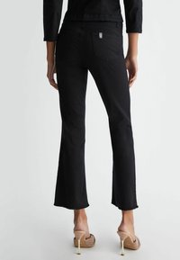 Jeans noirs évasés avec un ourlet brut et des poches arrière, associés à des talons ouverts beiges avec un design texturé et des accents de talon transparent.