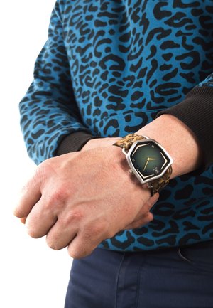 Grøn hexagonal ur ansigt med sølv hardware, leopardmønstret rem, båret på håndleddet, alongside en blå leopardprint sweater.